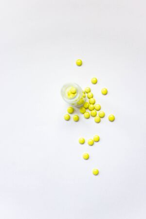 Yellow pills spilling out of bottle on white background with copy space. Flat lay. Drug production in pharmaceutical industry concept. Healthcare and medicine background.の写真素材