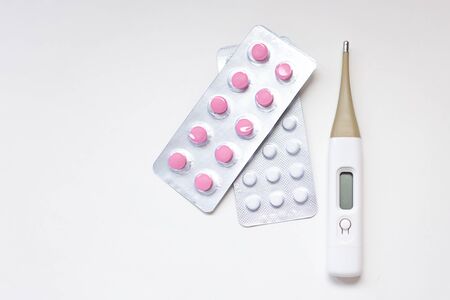 Colorful antibiotics capsule pills pink and white color in blister pack and thermometer on white...