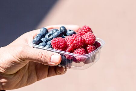 the guy is holding a tray of raspberries and blueberries. Vitamin-rich fruits are packaged in boxes....