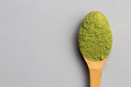 Brown wooden spoon with tea of a match on a light gray background. Matcha green tea in powder. Copy...