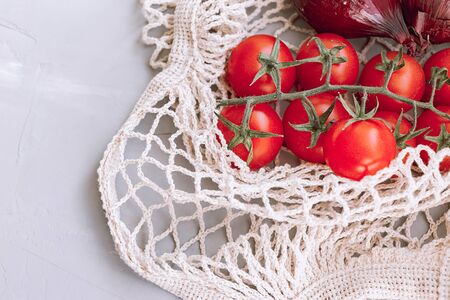 Zero waste and eco friendly shopping. Eco friendly mesh bag with organic vegetables (tomato and onion) on a grey background . Top view.の写真素材