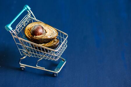 Spoiled and rotten avocado with mold in a mini food cart on a blue background.  Two halves of moldy...
