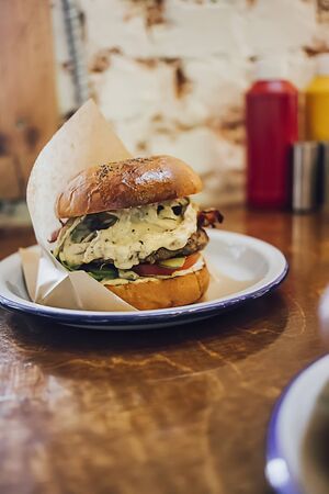 Beef burger with mushrooms, meatballs, tomato, cheese sauce and lettuce on wooden background. Close...