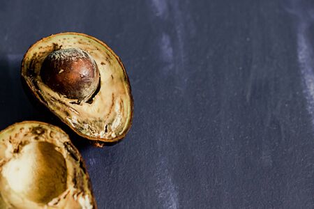 A rotten spoiled avocado fruit cut in half on blue background. One slice with core. Stop wasting food. Copy spacy.の写真素材