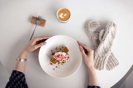 The girl holds a plate with a cake, next to the mittens. The view from the top. Concept of winter, warmth, holidays, events. Soft focus.の写真素材