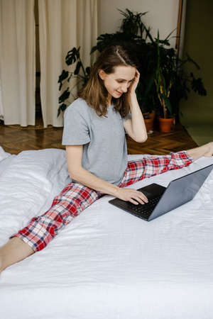 Pretty slim woman doing stretching online infront of laptop in bedroom. Stay home concept.の写真素材