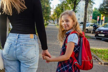 Adorable cute little girl feeling excited about going back from school with her mother by the hand. A pretty girl with a backpack walks on the street with her mother.の写真素材