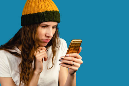 Woman doing Video Call using a phone isolated on blue background. Portrait of surprised upset sad thoughtful minded female looking phone trying to understand information.の写真素材