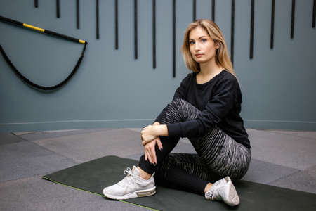 Attractive happy woman sitting on the floor after exercise on gym background. Concept of slim and...