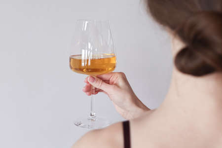 Back view young woman holding and tasting a glass of white wine. Focus on a glass of wine. Copy spaceの写真素材