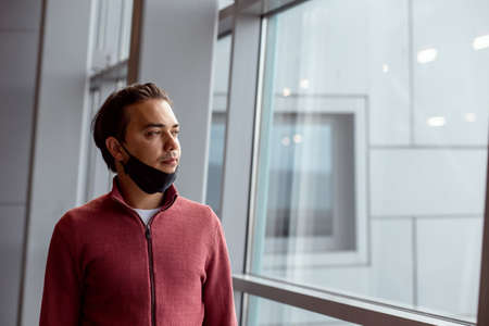 A guy with a protection black medical mask on the face at the airport is waiting for flight. Air travel during the  pandemic. Copy space.の写真素材