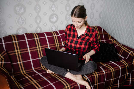 Happy european female student in casual outfit, smiling while using laptop to learning online sitting at home interior. Self education in terms of quarantine.の写真素材