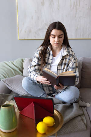 girl reading book, doing homework using tablet