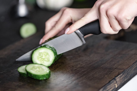 woman hand cutting cucumber on chopping woodの写真素材