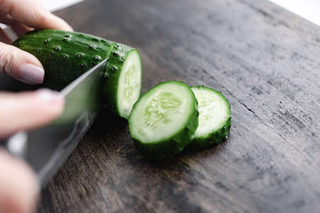 woman hand cutting cucumber on chopping woodの写真素材