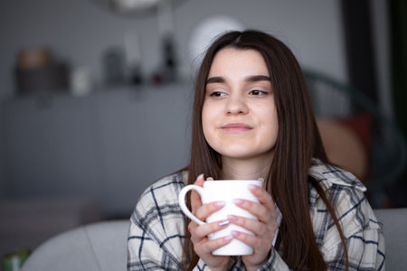 Women sitting in cozy couch with blanket with coffee. Woman have relax Enjoying quiet lifestyle indoor at home with cup of tea. Copy space.の写真素材