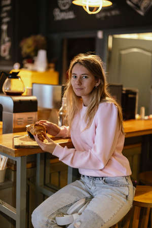 A beautiful woman sitting in a cafe, enjoying a croissant.