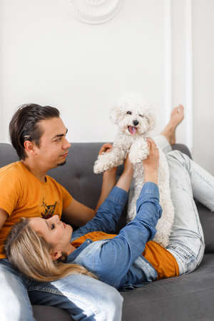 portrait of a happy family - a guy, a girl and a Bichon dog lie on the couch and hugging. family and...