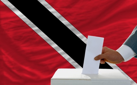 man putting ballot in a box during elections in trinidad tobago in front of flagの写真素材