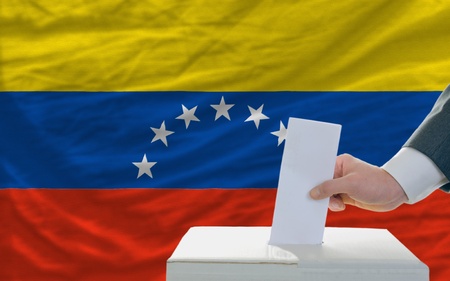 man putting ballot in a box during elections in venezuela in front of flagの写真素材