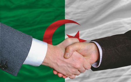 two businessmen shaking hands after good business investment  agreement in algeria, in front of flagの写真素材