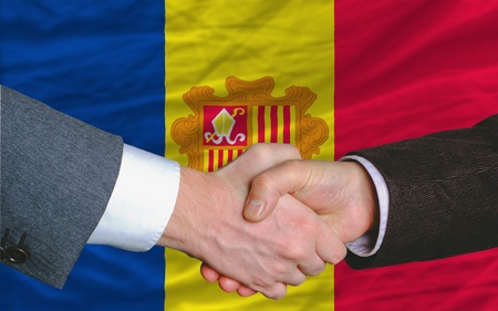 two businessmen shaking hands after good business investment  agreement in andora, in front of flagの写真素材