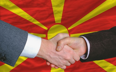 two businessmen shaking hands after good business investment  agreement in macedonia, in front of flagの写真素材