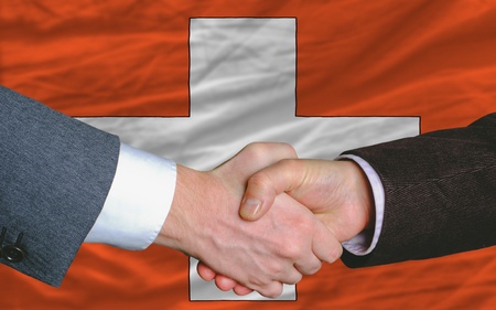 two businessmen shaking hands after good business investment  agreement in swiss, in front of flagの写真素材