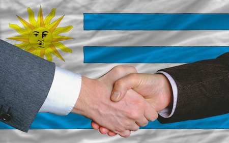 two businessmen shaking hands after good business investment  agreement in uruguay, in front of flagの写真素材