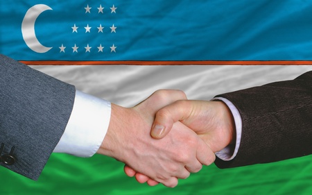 two businessmen shaking hands after good business investment  agreement in uzbekistan, in front of flagの写真素材