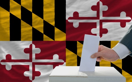 man putting ballot in a box during elections  in front of flag american state of marylandの写真素材