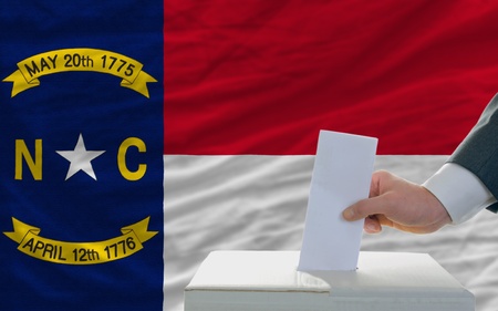 man putting ballot in a box during elections  in front of flag american state of north dakotaの写真素材