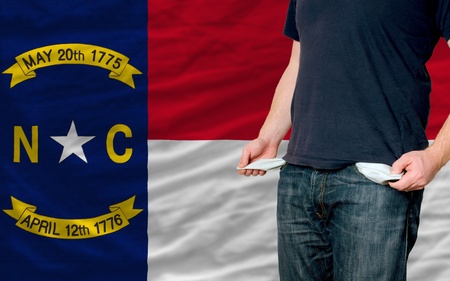 poor man showing empty pockets in front of american state of north carolina flagの写真素材