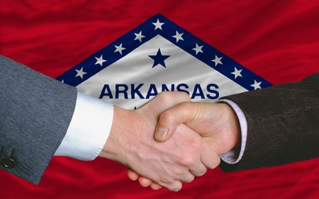 two businessmen shaking hands after good business investment  agreement in america, in front US state flag of arkansasの写真素材