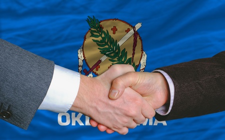 two businessmen shaking hands after good business investment agreement in front US state flag of oklahomaの写真素材