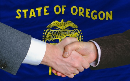 two businessmen shaking hands after good business investment agreement in front US state flag of oregonの写真素材