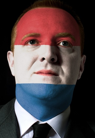 High key portrait of a serious businessman or politician whose face is painted in national colors of holland flagの写真素材