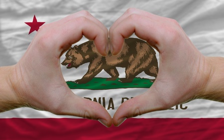 Gesture made by hands showing symbol of heart and love over us state flag of californiaの写真素材