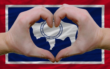 Gesture made by hands showing symbol of heart and love over us state flag of wyomingの写真素材