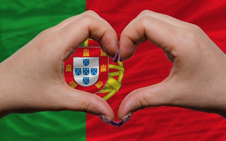 Gesture made by hands showing symbol of heart and love over national portugal flag