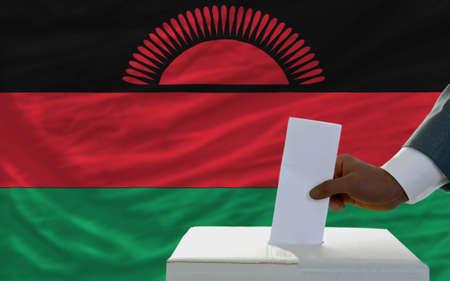 man putting ballot in a box during elections  in front of national flag of malawiの写真素材