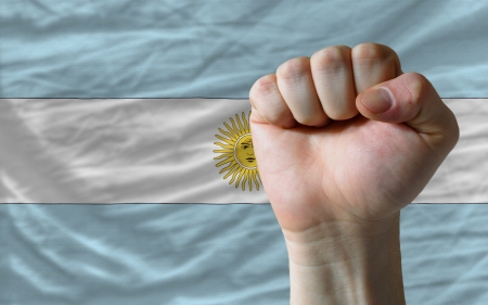 complete national flag of argentina covers whole frame, waved, crunched and very natural looking. In front plan is clenched fist symbolizing determinationの写真素材
