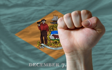 complete american state of delaware flag covers whole frame, waved, crunched and very natural looking. In front plan is clenched fist symbolizing determinationの写真素材