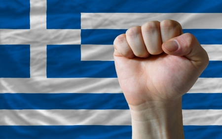 complete national flag of greece covers whole frame, waved, crunched and very natural looking. In front plan is clenched fist symbolizing determinationの写真素材