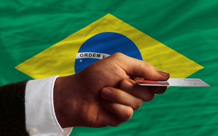 man stretching out credit card to buy goods in front of complete wavy national flag of brazilの写真素材
