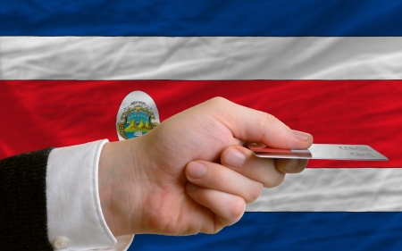 man stretching out credit card to buy goods in front of complete wavy national flag of costa ricaの写真素材