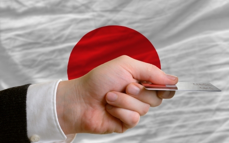 man stretching out credit card to buy goods in front of complete wavy national flag of japanの写真素材