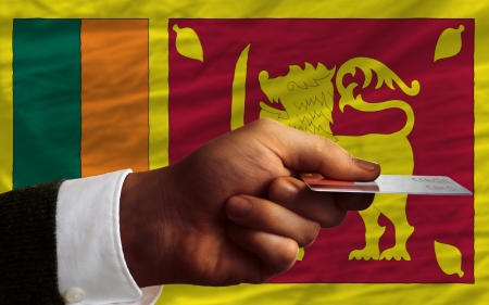 man stretching out credit card to buy goods in front of complete wavy national flag of sri lankaの写真素材