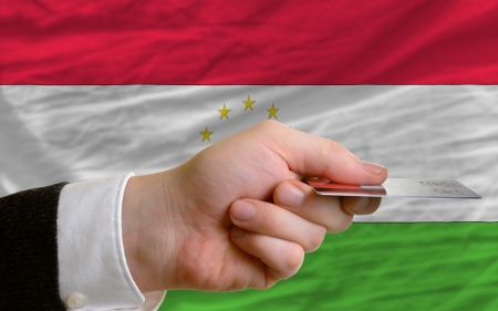 man stretching out credit card to buy goods in front of complete wavy national flag of tajikistanの写真素材