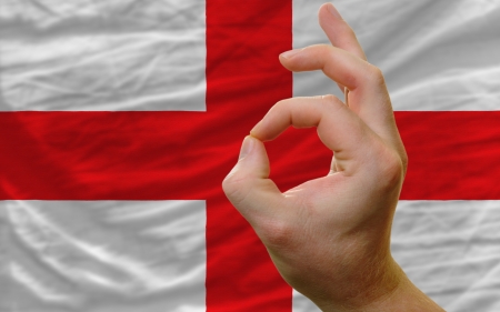 man showing excellence or ok gesture in front of complete wavy england national flag of  symbolizing best quality, positivity and succesの写真素材